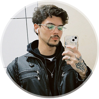 Foto de André Xavier, com barba, usando óculos, camisa cinza, moletom e jaqueta pretas.